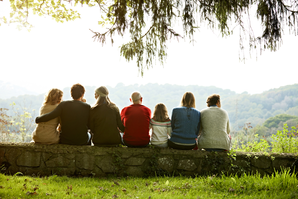 Bildet viser syv personer i ulik alder bakfra. De sitter på en trestamme og ser utover fjellene. De er i familie. Foto